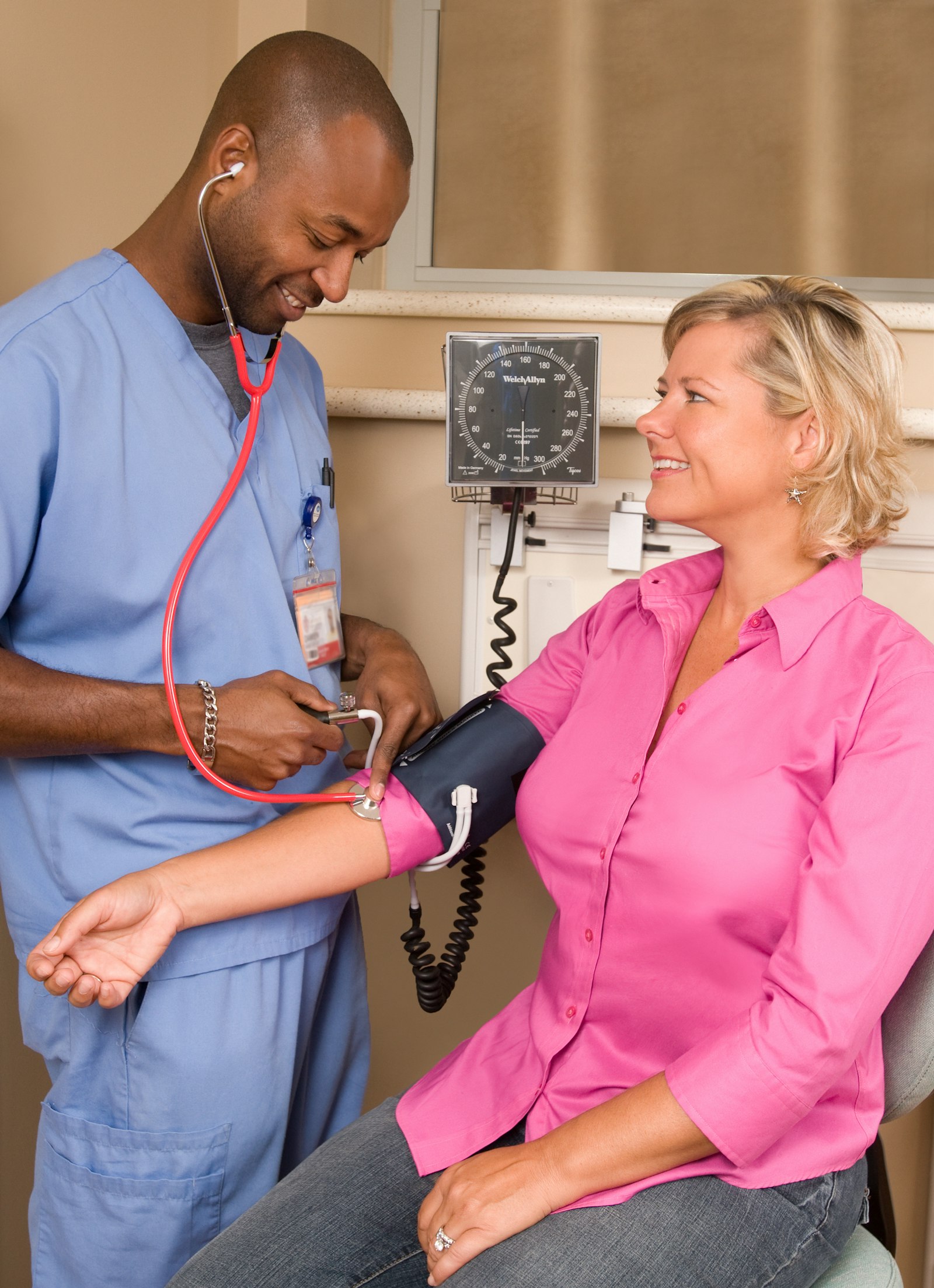 A healthcare worker in blue scrubs checking a woman's blood pressure
