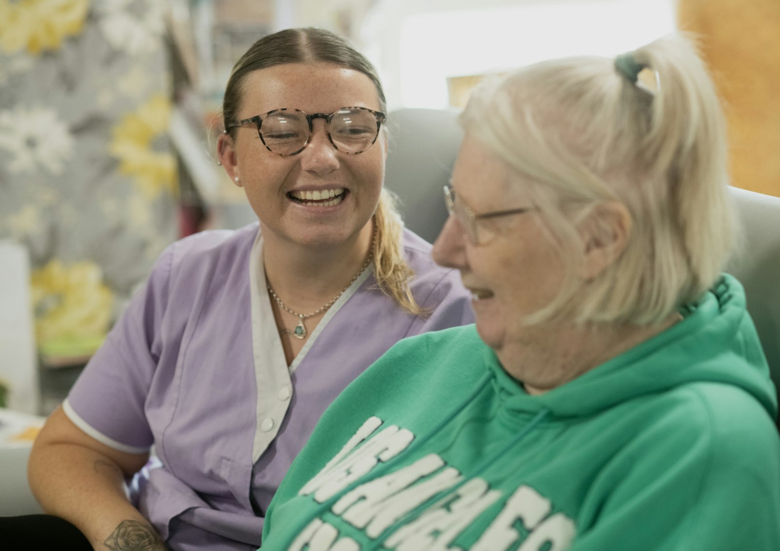 A young caregiver laughing with an elderly woman