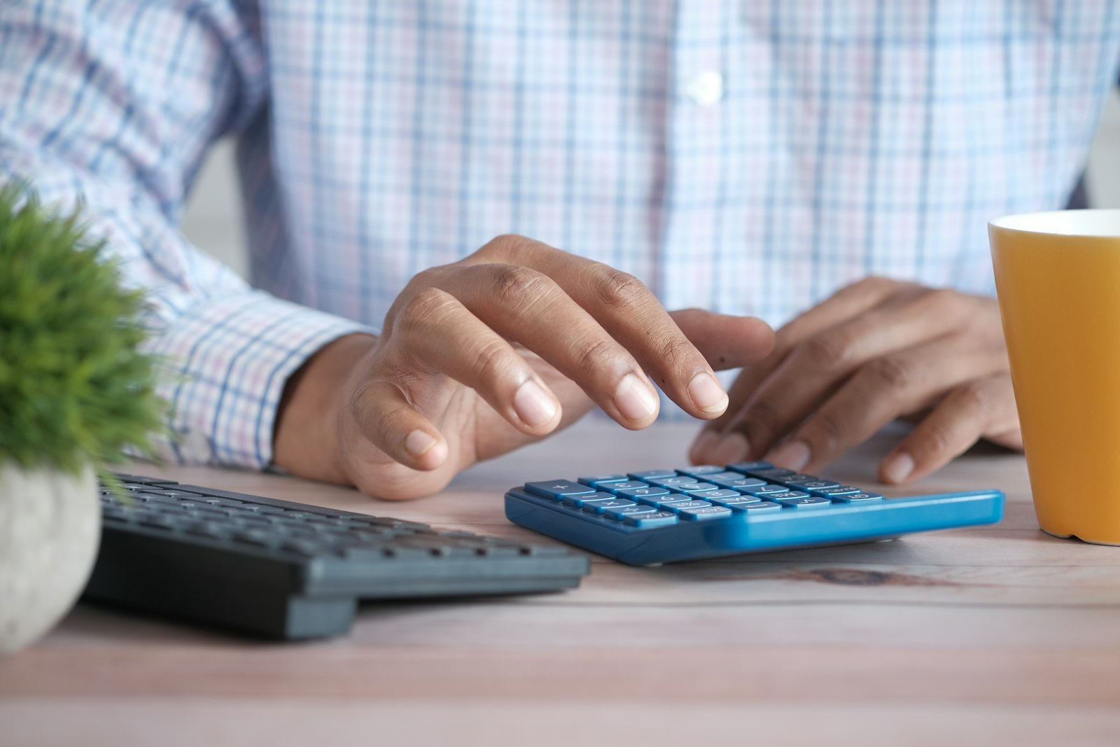 Hands using a calculator next to a coffee mug